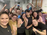 MNI Abschlussfoto Eine große Gruppe von Teilnehmenden des Programms „Mein neues Ich #Neustart“ posiert nach einer Trainingseinheit fröhlich in einem Fitnessraum und zeigt Peace-Zeichen sowie Daumen nach oben.