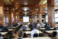 Vollzeit-Technikerstart in der Bibliothek der Eckert Schulen: Begrüßung durch Geschäftsführer und Schulleiter Markus Johannes Zimmermann Das Foto zeigt die Bibliothek der Eckert Schulen, in der zahlreiche Teilnehmende der Vollzeit-Weiterbildung „Staatlich geprüfter Techniker“ sitzen. In dem großen, holzvertäfelten Saal stehen Tische und Stühle in Reihen. Die Teilnehmenden blicken nach vorne zu einer Leinwand, auf der eine Präsentation gezeigt wird. Dort begrüßt Geschäftsführer und Schulleiter Markus Johannes Zimmermann die neuen Vollzeit-Techniker offiziell zum Start ihres Lehrgangs.