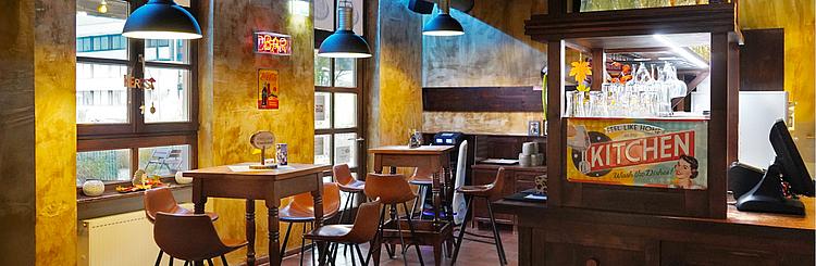 Campus Sports Bar Gemütlich eingerichtete Campus Sports Bar mit Holztischen, braunen Lederstühlen und stimmungsvoller Beleuchtung.