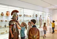 Mitmachen und entdecken: Geschichte wird lebendig Kinder probieren römische Rüstung in einer Museumsausstellung aus und betrachten Ausstellungsstücke.