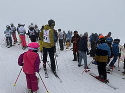 Mehrere Teilnehmende der Rotary Skimeisterschaft stehen startbereit auf der Piste. Unter den Teilnehmenden befinden sich sowohl Erwachsene als auch Kinder. Das Wetter ist auffällig neblig.