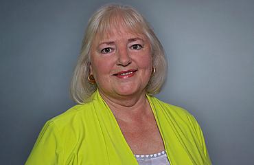 Olga Nasseide – Leitung medizinischer Dienst am BFW Eckert Eine Frau mit schulterlangem, silbergrauem Haar und freundlichem Lächeln trägt ein auffällig limonengelbes Oberteil. Sie steht vor einem neutralen Hintergrund und blickt direkt in die Kamera.