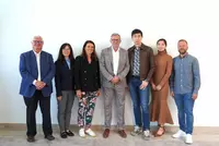 Demaridea_Gruppenbild Sieben Personen stehen vor einer weißen Wand und schauen freundlich in die Kamera.