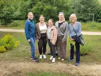 Exkursion in den Heilkräutergarten Fünf Frauen stehen lächelnd auf einem Weg im Grünen, Hintergrund mit Bäumen und Wiese